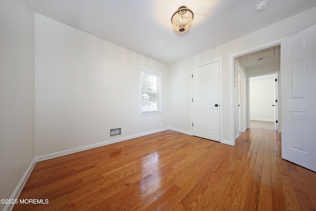 spare room with attic access, light wood-style floors, and baseboards