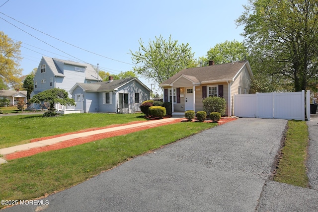 bungalow-style house with fence, a chimney, driveway, and a front lawn