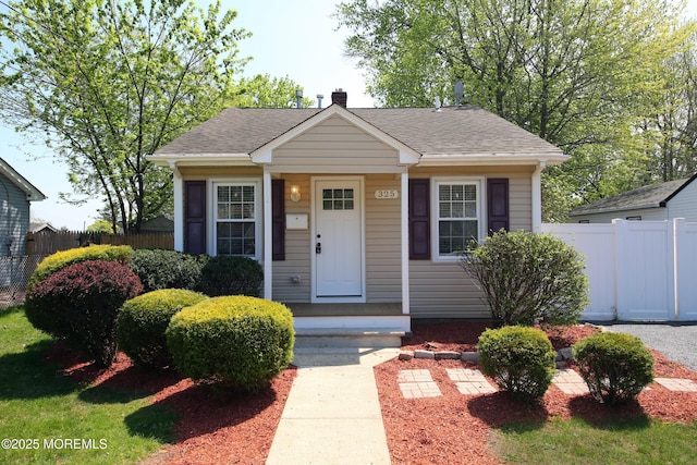 bungalow-style home with a chimney, fence, and a shingled roof