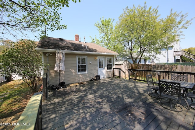 exterior space with an outdoor structure, a wooden deck, a storage unit, a chimney, and outdoor dining space
