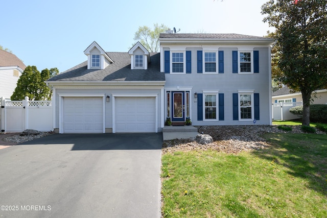 colonial house featuring driveway, a shingled roof, a front yard, an attached garage, and fence