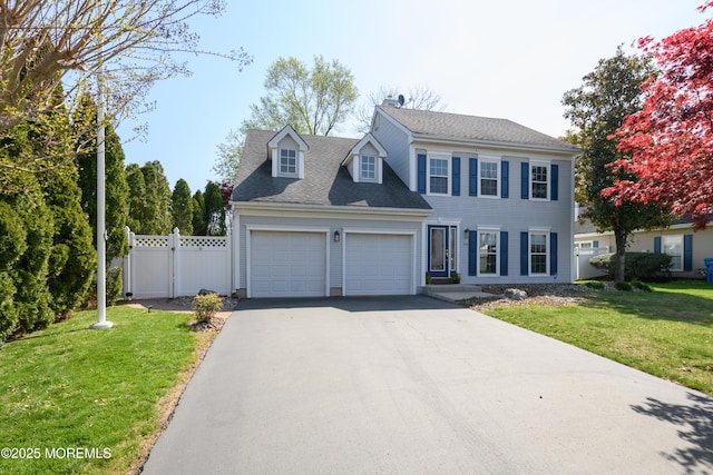 colonial house featuring driveway, roof with shingles, a front yard, fence, and a garage