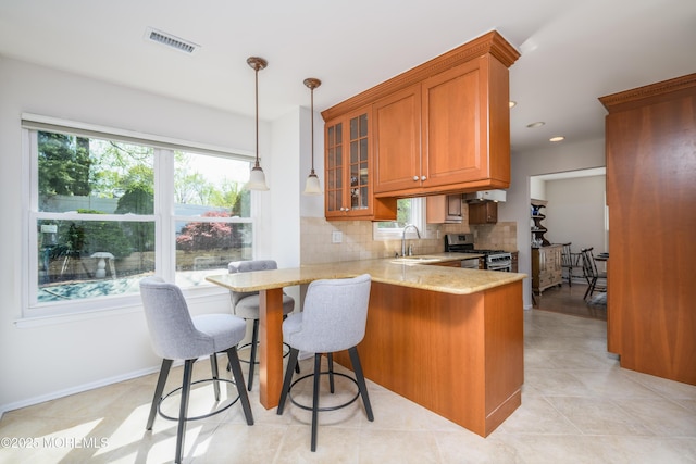kitchen featuring light stone counters, a wealth of natural light, brown cabinets, visible vents, and stainless steel gas range