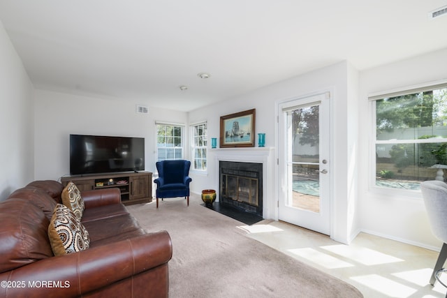 living area featuring visible vents, a fireplace with flush hearth, a wealth of natural light, and light colored carpet