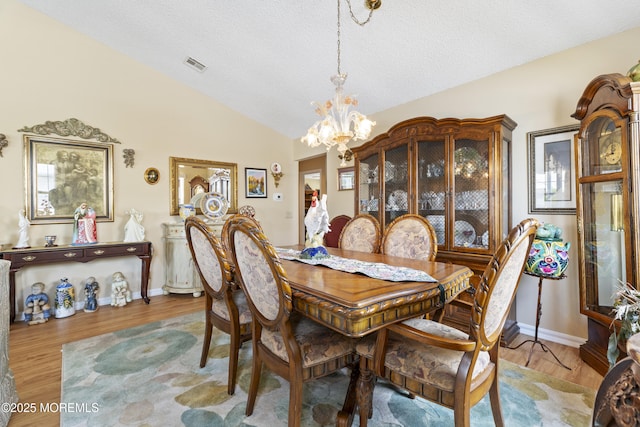 dining area featuring wood finished floors, an inviting chandelier, vaulted ceiling, visible vents, and a textured ceiling