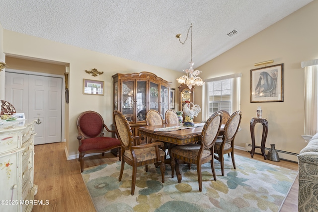 dining room featuring an inviting chandelier, a baseboard heating unit, light wood finished floors, a textured ceiling, and lofted ceiling