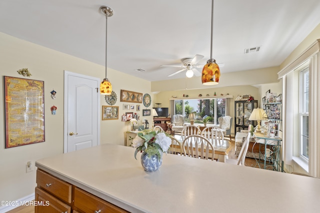 kitchen with hanging light fixtures, brown cabinetry, light countertops, visible vents, and a ceiling fan