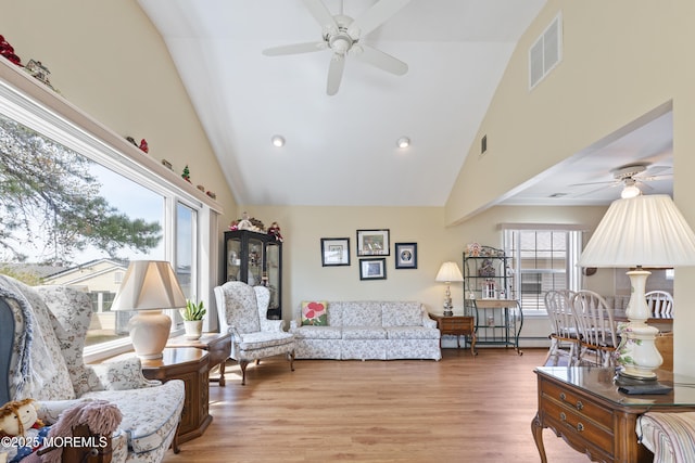 living room with a wealth of natural light, visible vents, a ceiling fan, and high vaulted ceiling