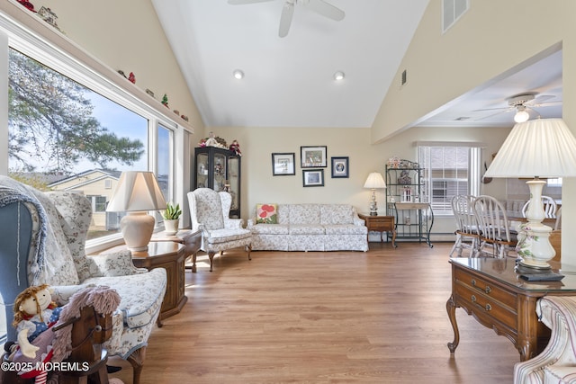 living area featuring visible vents, light wood finished floors, ceiling fan, and high vaulted ceiling