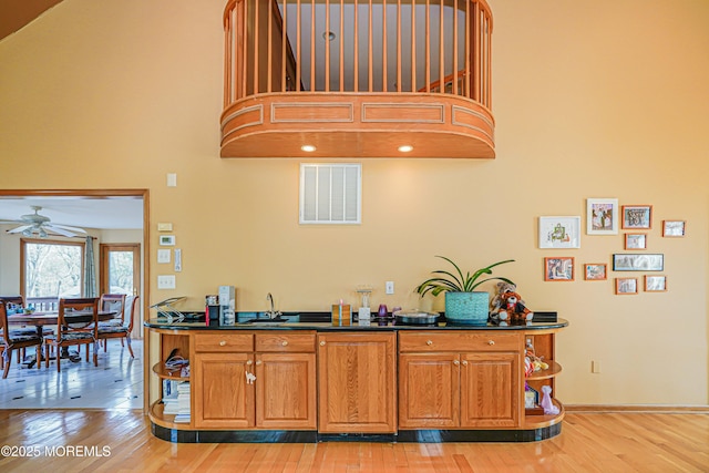kitchen featuring dark countertops, a high ceiling, a ceiling fan, light wood-type flooring, and visible vents