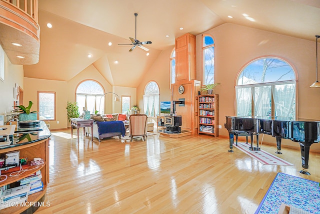 living area with a wood stove, ceiling fan, high vaulted ceiling, light wood-type flooring, and recessed lighting