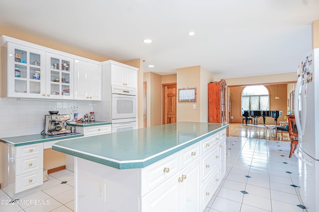 kitchen with a center island, tasteful backsplash, glass insert cabinets, white appliances, and light tile patterned flooring