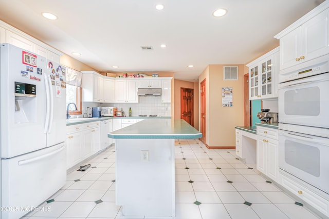 kitchen with a sink, white appliances, recessed lighting, under cabinet range hood, and visible vents