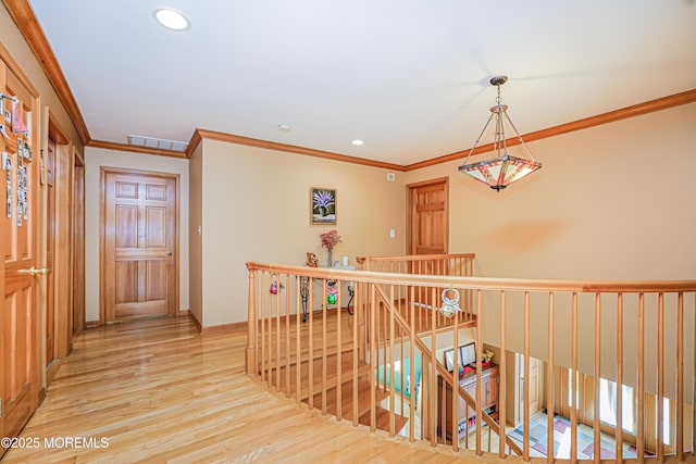 hall featuring visible vents, crown molding, wood finished floors, and an upstairs landing
