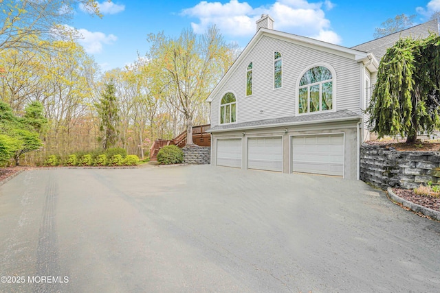 view of side of home featuring driveway, a chimney, stairs, and a garage