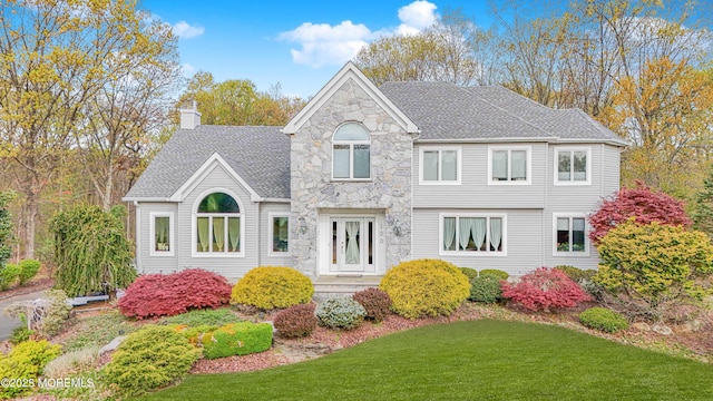 exterior space with stone siding, roof with shingles, a chimney, and a front yard