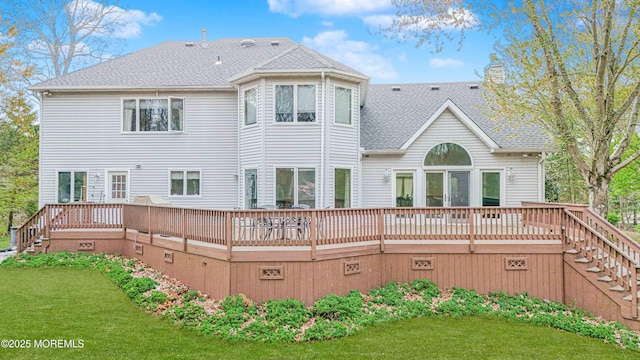 rear view of house featuring a wooden deck, a chimney, stairs, a shingled roof, and a lawn