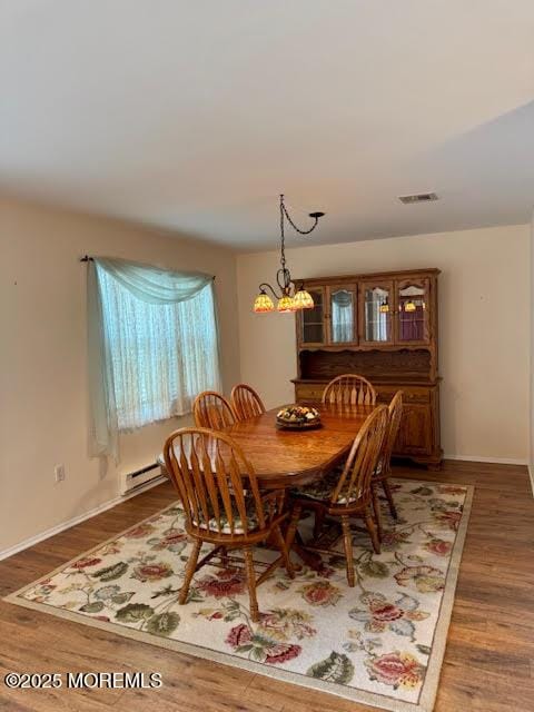 dining space featuring wood finished floors, visible vents, baseboard heating, and baseboards
