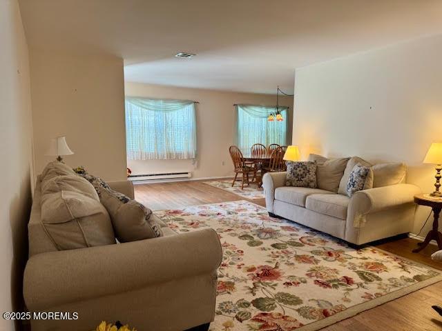 living area with visible vents, wood finished floors, a notable chandelier, and a baseboard heating unit