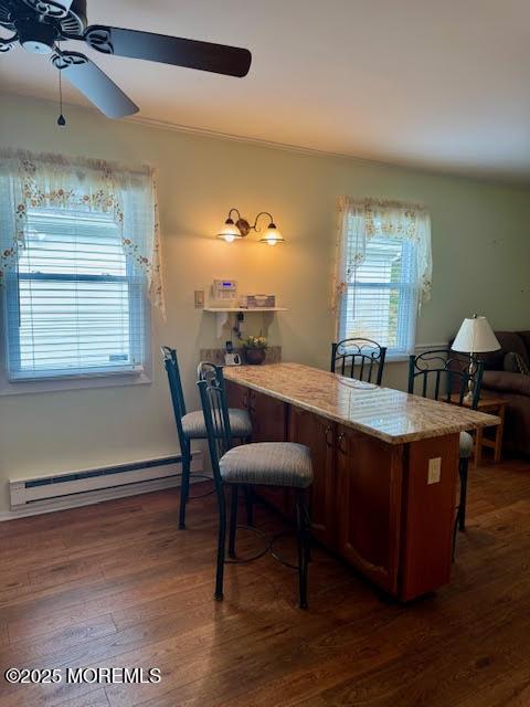 office area with a healthy amount of sunlight, a ceiling fan, dark wood-style floors, and baseboard heating