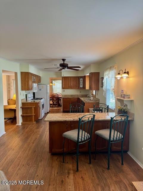 kitchen with dark wood-type flooring, a peninsula, white range with gas stovetop, and brown cabinetry