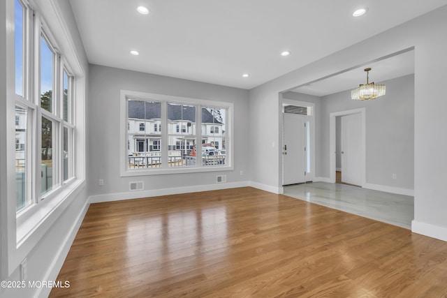 unfurnished room featuring wood finished floors, visible vents, a healthy amount of sunlight, and a chandelier