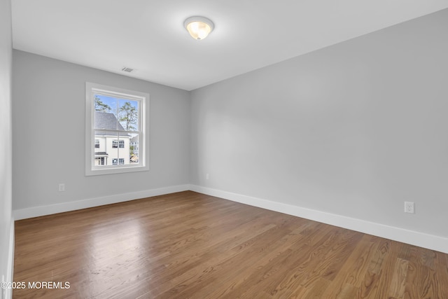 unfurnished room with baseboards, visible vents, and wood finished floors