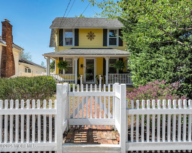 view of front of home with roof with shingles, covered porch, and a fenced front yard