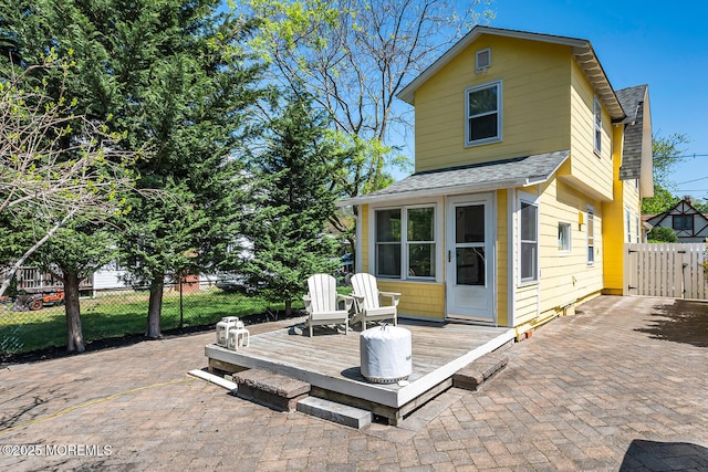 rear view of house with roof with shingles, fence, a wooden deck, a gate, and a patio