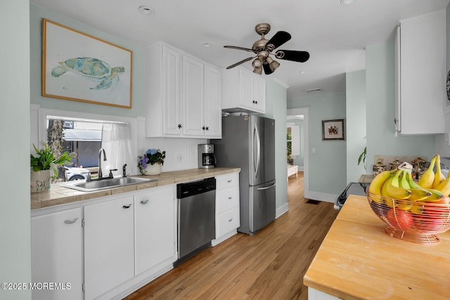 kitchen featuring appliances with stainless steel finishes, a sink, light wood finished floors, a ceiling fan, and white cabinetry