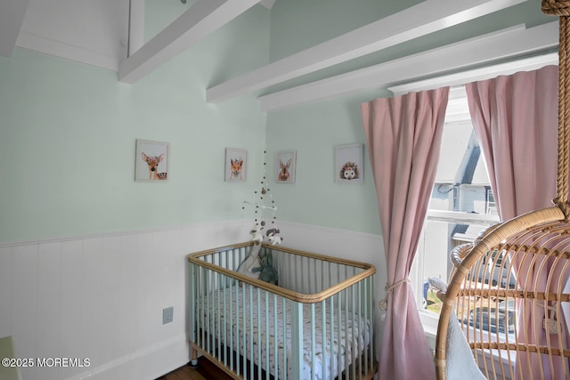 bedroom featuring a nursery area and a wainscoted wall