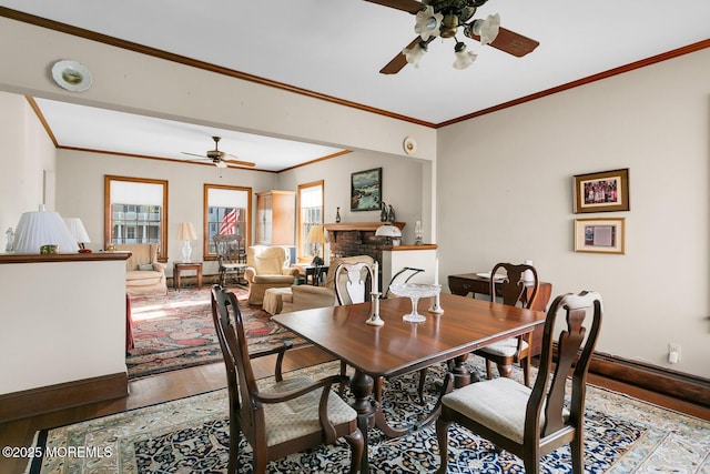 dining room with ornamental molding, a fireplace, baseboards, hardwood / wood-style flooring, and a ceiling fan