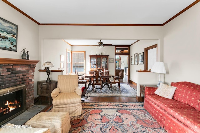 living area with crown molding, a brick fireplace, wood finished floors, baseboards, and ceiling fan