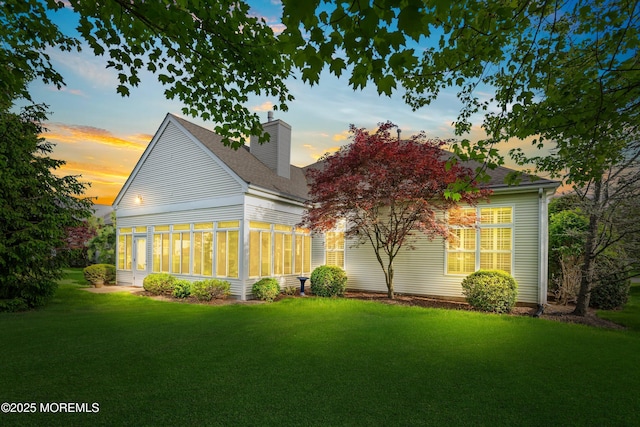 rear view of house with roof with shingles, a yard, a chimney, and a sunroom