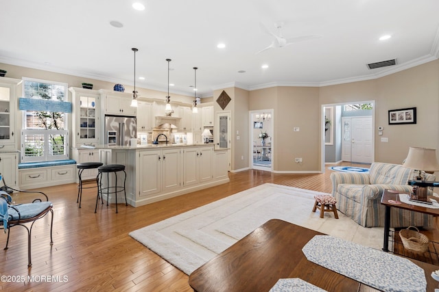 living area with a ceiling fan, recessed lighting, light wood-style flooring, ornamental molding, and baseboards