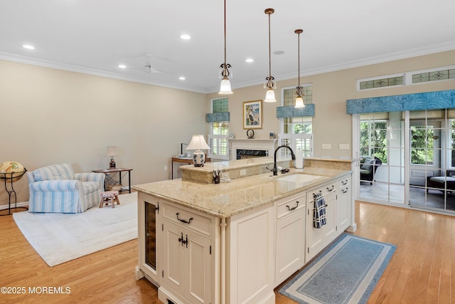 kitchen featuring a sink, open floor plan, crown molding, light wood-style flooring, and a fireplace