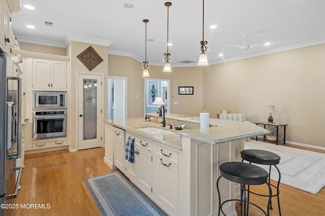 kitchen featuring stainless steel appliances, a sink, ornamental molding, white cabinets, and a kitchen breakfast bar