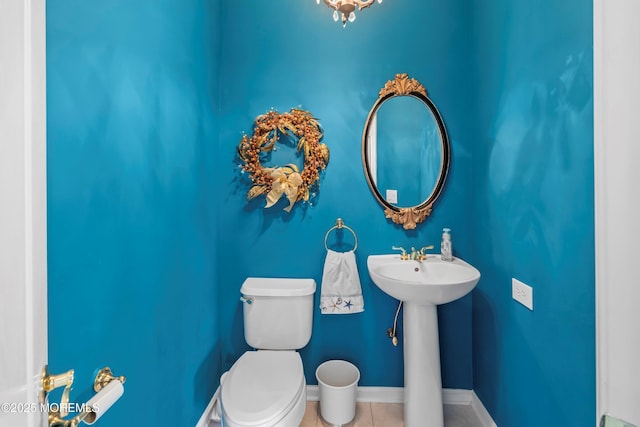 half bath featuring toilet, tile patterned flooring, baseboards, and a sink