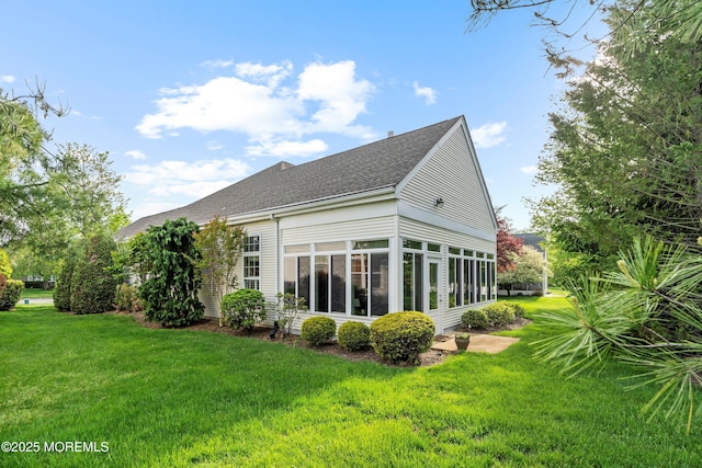 back of property featuring roof with shingles, a sunroom, and a lawn