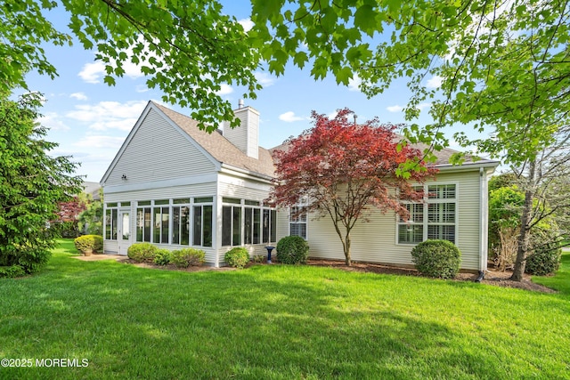 back of property with a shingled roof, a yard, a sunroom, and a chimney
