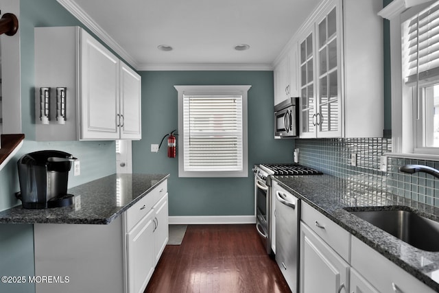 kitchen with crown molding, white cabinets, a sink, stainless steel appliances, and glass insert cabinets