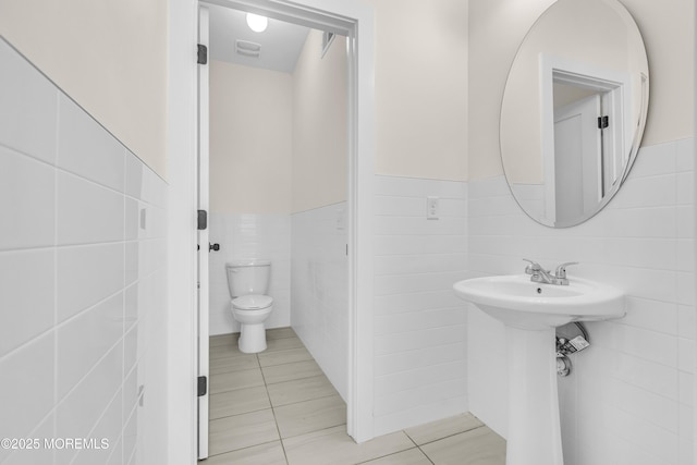bathroom featuring tile walls, wainscoting, toilet, and tile patterned flooring