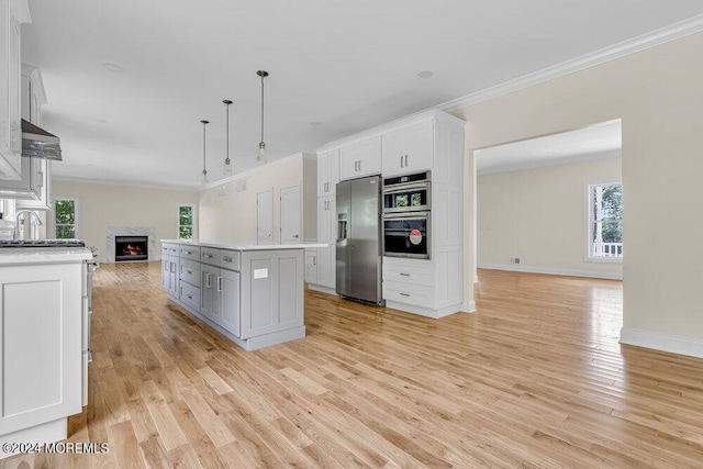 kitchen with a warm lit fireplace, ornamental molding, stainless steel refrigerator with ice dispenser, and open floor plan
