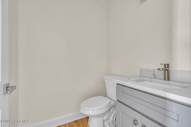 half bathroom featuring vanity, baseboards, wood finished floors, and toilet
