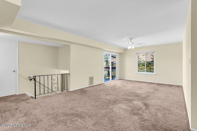 carpeted spare room with visible vents, a ceiling fan, and baseboards