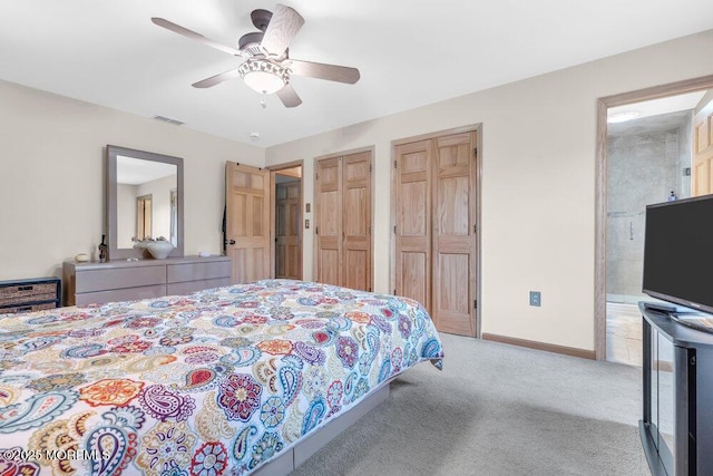 carpeted bedroom with ceiling fan, visible vents, baseboards, two closets, and connected bathroom