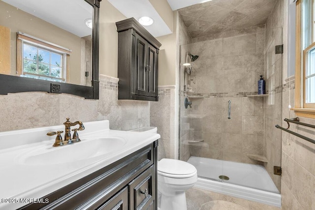 bathroom with vanity, toilet, tile walls, a wainscoted wall, and a stall shower