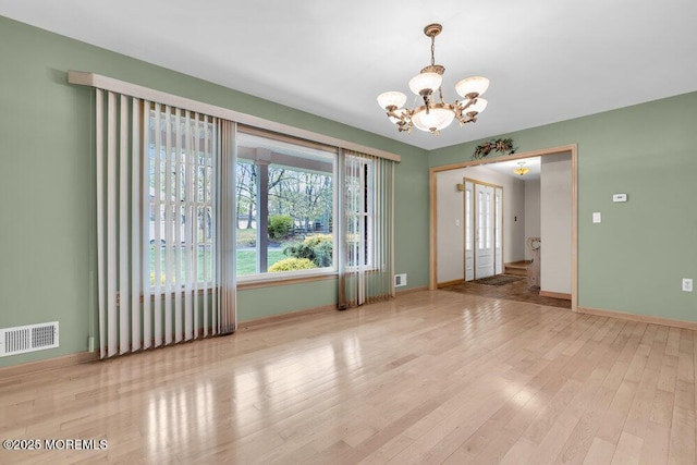 empty room featuring a notable chandelier, visible vents, baseboards, and wood finished floors