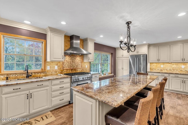 kitchen featuring light stone countertops, a sink, a chandelier, premium appliances, and wall chimney exhaust hood