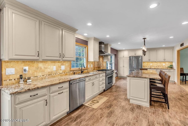 kitchen with light stone countertops, wall chimney range hood, tasteful backsplash, a sink, and stainless steel appliances